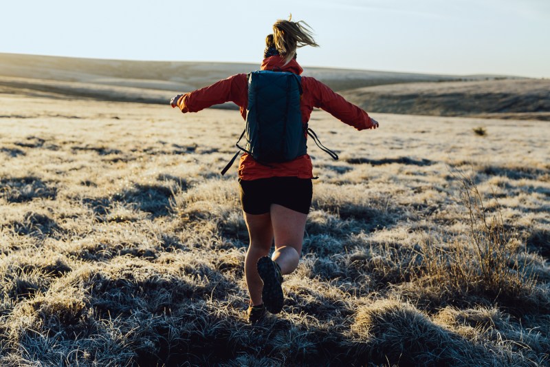一个女人脱机穿红色夹克短裤并背负小蓝背包