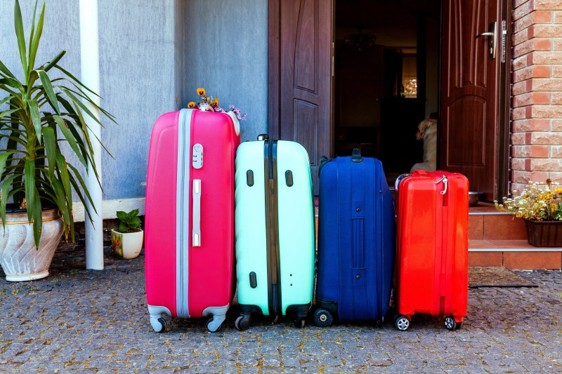 四色手提箱站在房子前家车旁的行李准备度假