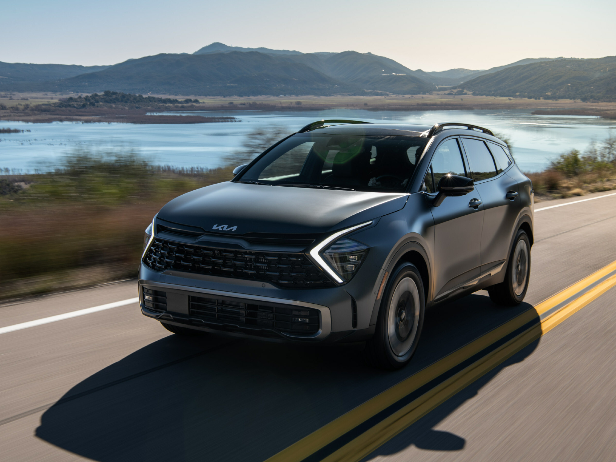 2024Kia运动gePHEV前端四分之三视图灰黄车后带水山