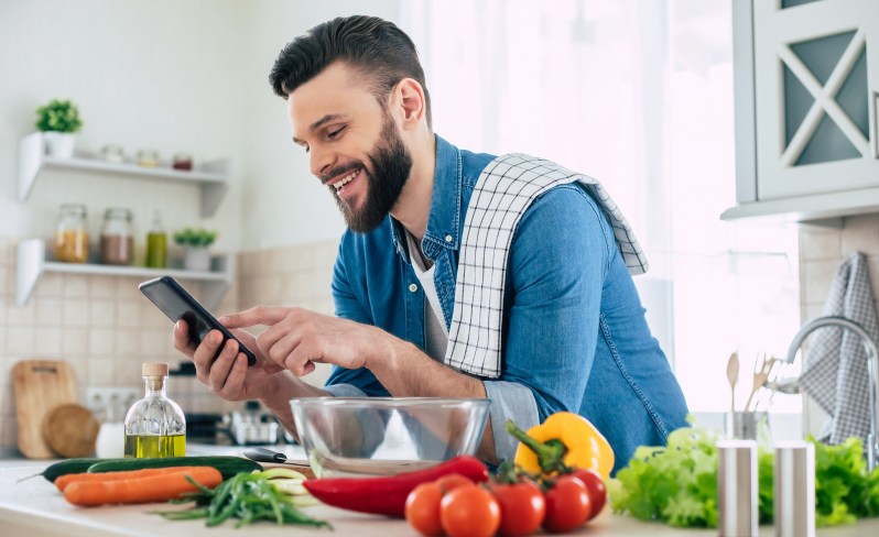 欢乐长胡子人使用智能手机 并准备素食健康早餐
