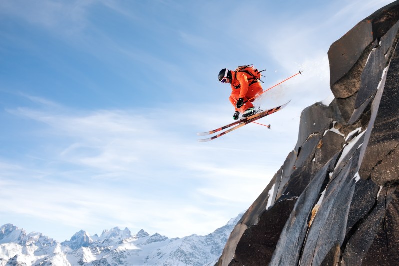 职业滑雪手从悬崖跳下蓝天空 留下山上积雪粉白雪山后台照片来自Elbrus山斜坡极端运动与娱乐概念 山冬复制空间